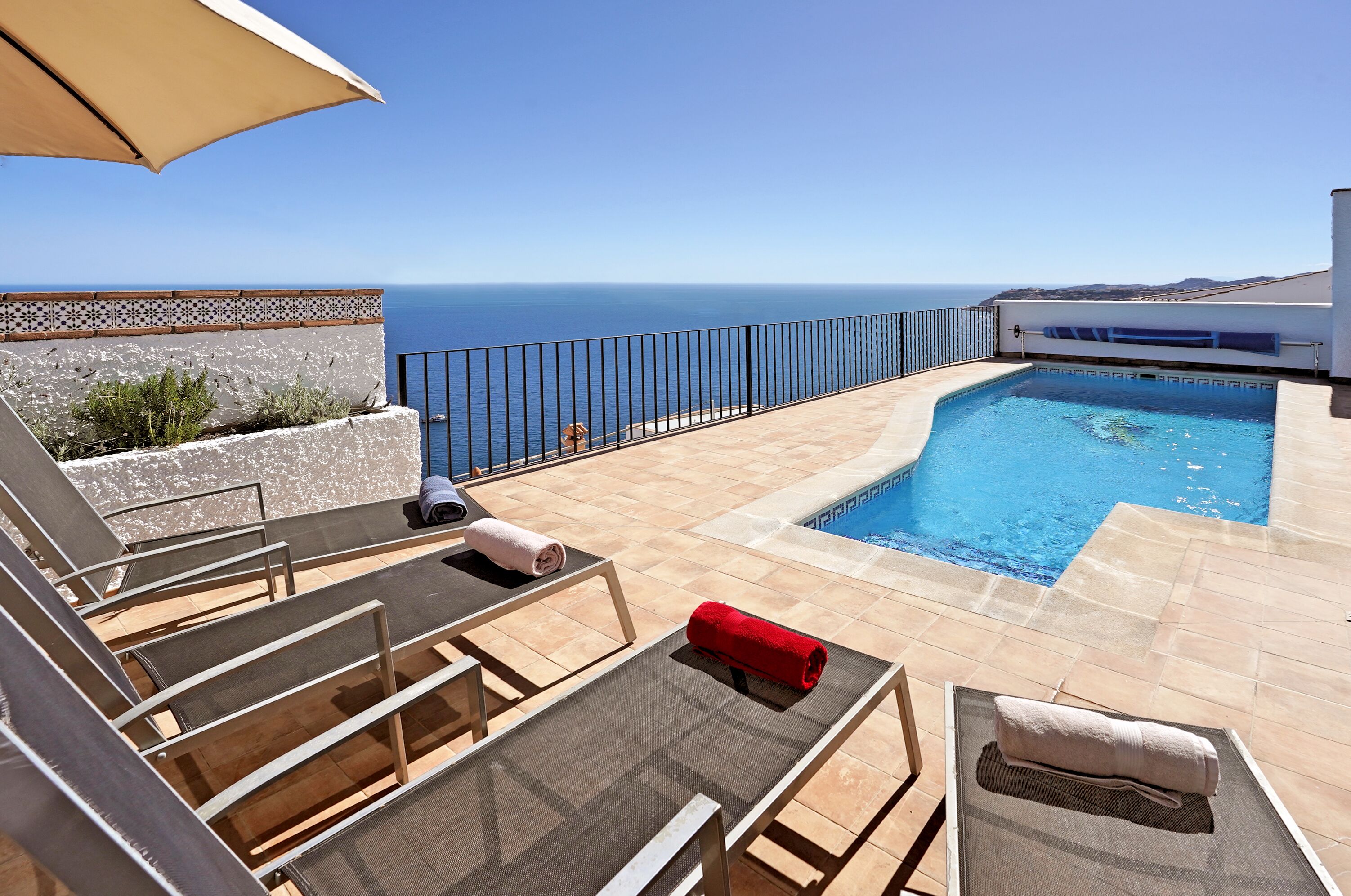 Une piscine sur le toit offrant une vue dégagée sur l’océan, entourée de chaises longues et d’une pergola.