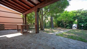 An outdoor patio area with stone flooring, wooden benches, and a pergola structure. - Villetta Agnese (San Teodoro)