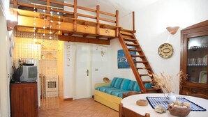 A cozy living room with a wooden staircase, a sofa, a dining table, and a television on a cabinet. - Villetta Agnese (San Teodoro)