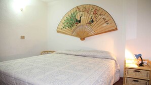 A bedroom with a bed, a wall-mounted fan with a peacock design, a bedside lamp, and a wicker nightstand. - Villetta Agnese (San Teodoro)