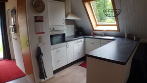 A compact kitchen with a built-in oven, a microwave, a sink, and a window with a view of greenery. - Gemütliches Ferienhaus am Twistesee im Ferienland Waldeck-frankenberg (Bad Arolsen-Wetterburg)
