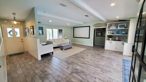 Un salon spacieux avec un canapé blanc, un pouf gris et un grand téléviseur à écran plat fixé au mur.