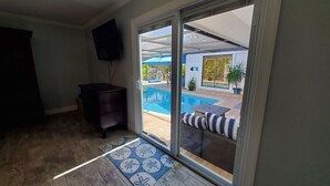 Une pièce dotée d’une porte-fenêtre coulissante donnant sur une piscine, d’un meuble en bois foncé et d’un tapis à motifs bleus.