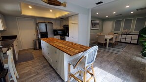 Une cuisine moderne avec des meubles blancs, un îlot central en bois et un coin repas comprenant une table et des chaises.