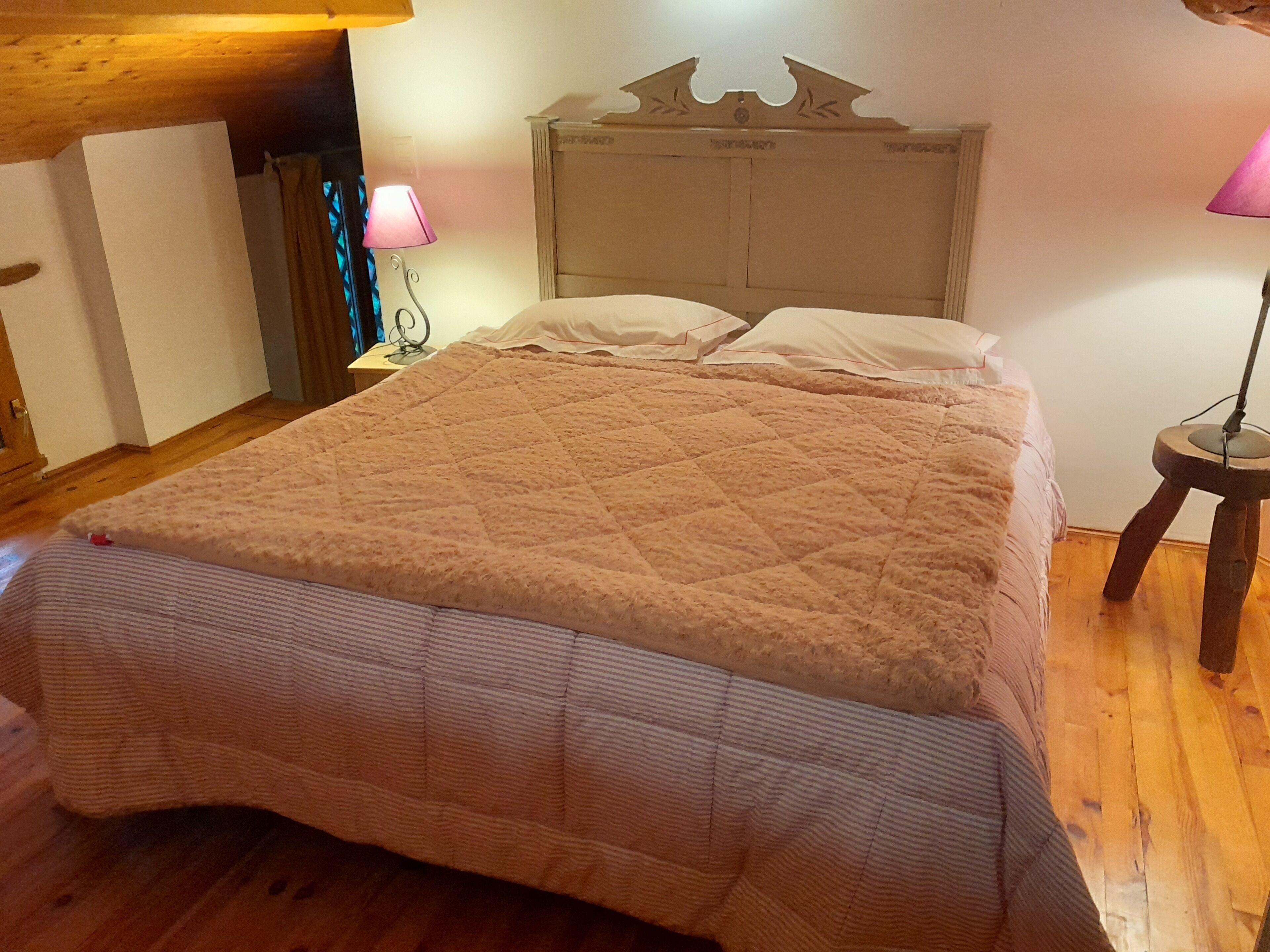 Un dormitorio con cama, suelo de madera y mesita de noche con lámpara.