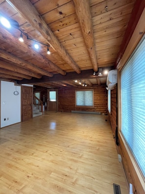 A spacious room with wooden floors and ceiling beams, large windows with blinds, and a door leading to another room. - New Listing! Spacious Montana cabin near downtown Whitefish (Whitefish)