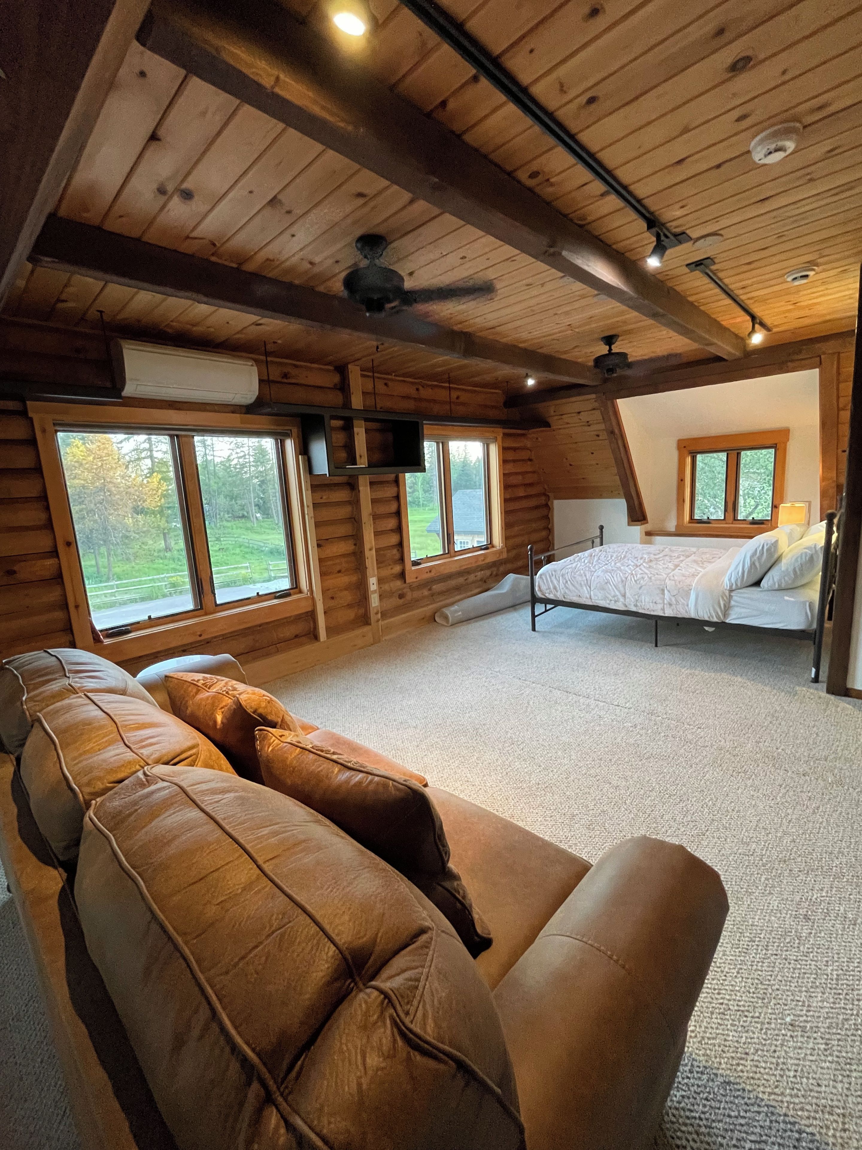 L'intérieur d'une cabane en rondins, avec un canapé, un lit et de grandes fenêtres.