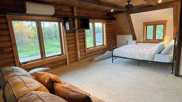L'intérieur d'une cabane en rondins, avec un canapé, un lit et de grandes fenêtres.