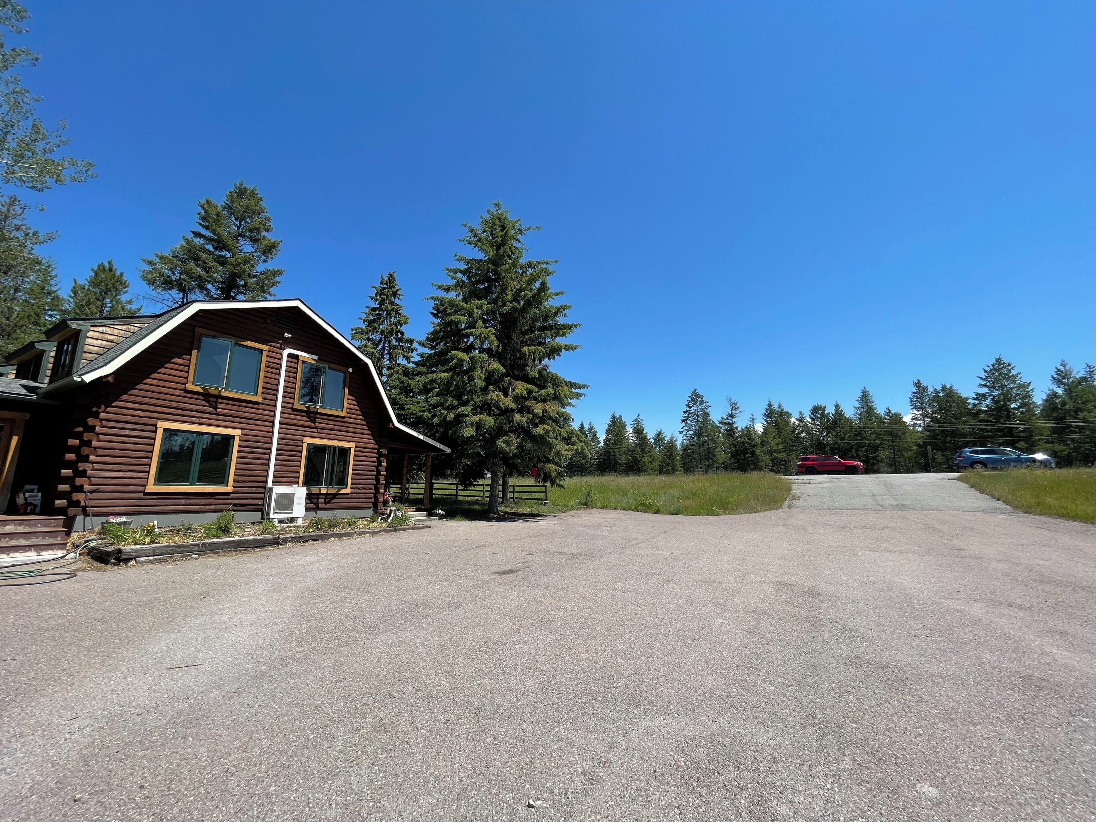 A log cabin with a gravel driveway and a red car parked in the distance.