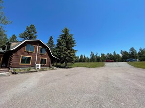 A log cabin with a gravel driveway and a red car parked in the distance.