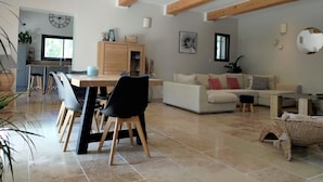 A spacious living area with a dining table, chairs, a sofa, and a coffee table. There is a kitchen area with a window and a cabinet. - Lou Mazet provençal à Eygalières - Private swimming pool (EYGALIERES)