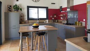 A modern kitchen with a central island, bar stools, a clock, and a window with a view. - Lou Mazet provençal à Eygalières - Private swimming pool (EYGALIERES)