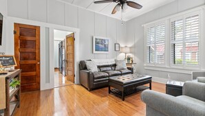 A spacious living room with hardwood floors, a leather sectional sofa, a grey armchair, and a ceiling fan. - .6 miles to Marktplatz - Walkable to Downtown - Firepit - (Fredericksburg)