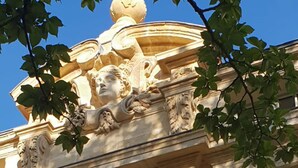 Um edifício com detalhes arquitetônicos clássicos, incluindo esculturas ornamentais e uma cúpula.
