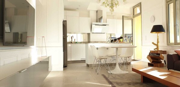 A modern kitchen with white cabinetry, a central island, and a dining area with white chairs.