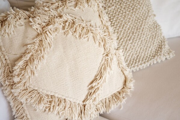 A close-up of a textured beige throw pillow with a fringe border, placed on a white surface.