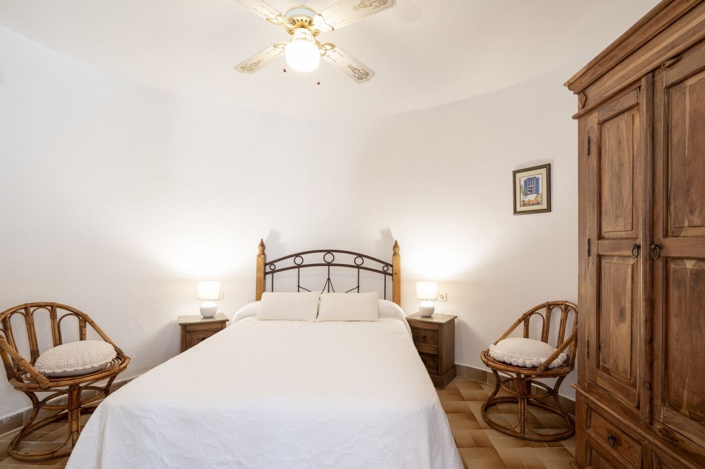 Un dormitorio con una cama, dos mesitas de noche con lámparas, un armario de madera y un ventilador de techo.