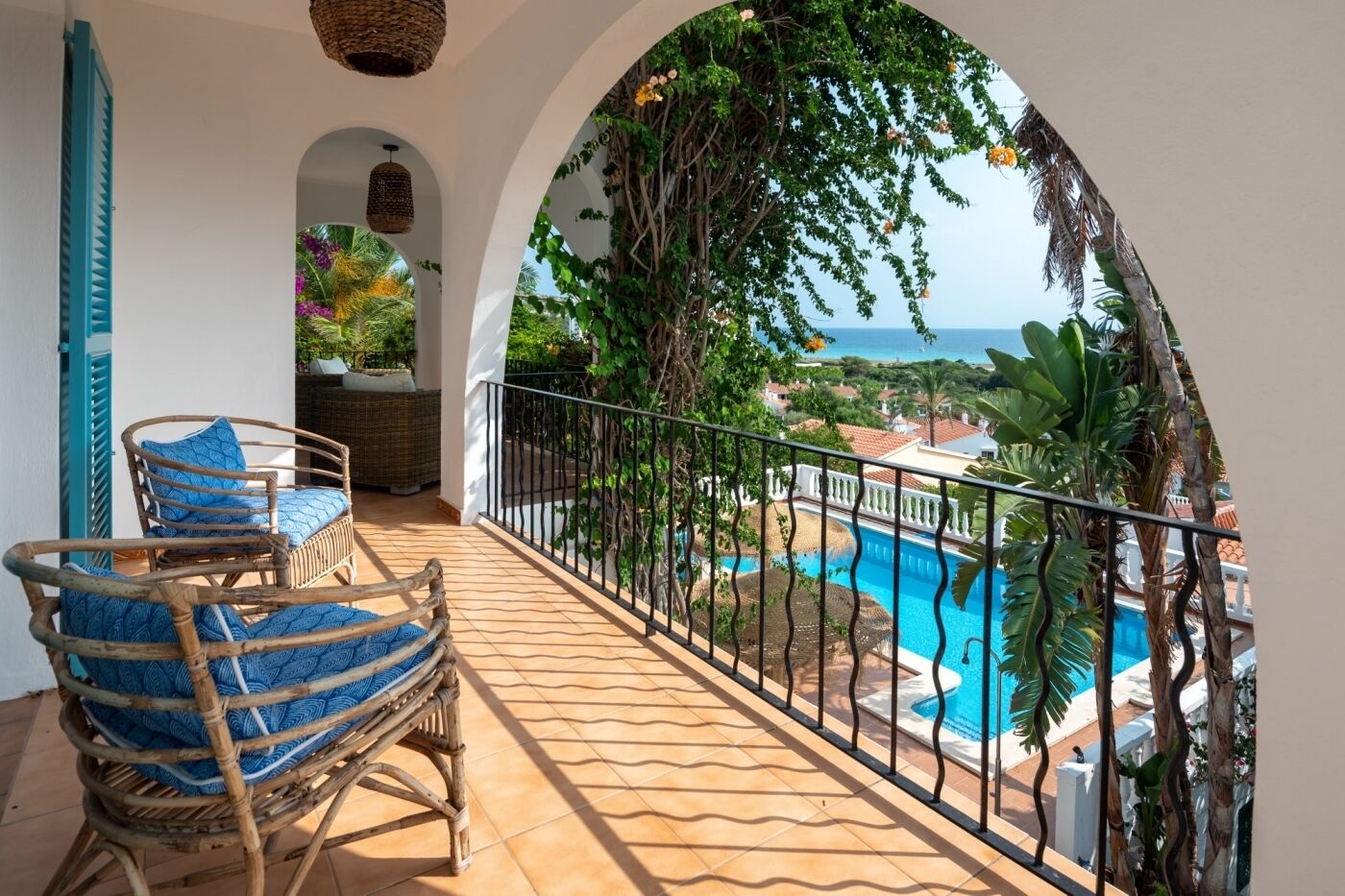 A balcony with wicker chairs, a view of a swimming pool, and a clear view of the sea.