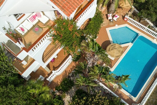 An aerial view of a resort with a swimming pool, lounge areas, and tropical landscaping. - Villa Margarita 85 by Book Menorca Villas (San Jaime Mediterráneo Alayor)
