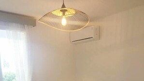 Une chambre avec un lit, un luminaire suspendu, un appareil de climatisation et une vue sur l’extérieur.