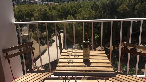 Un balcon avec une table en bois, deux chaises et une bouteille de vin.