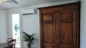 Une pièce comprenant un meuble en bois, une table à manger avec des chaises, une plante en pot et un appareil de climatisation.