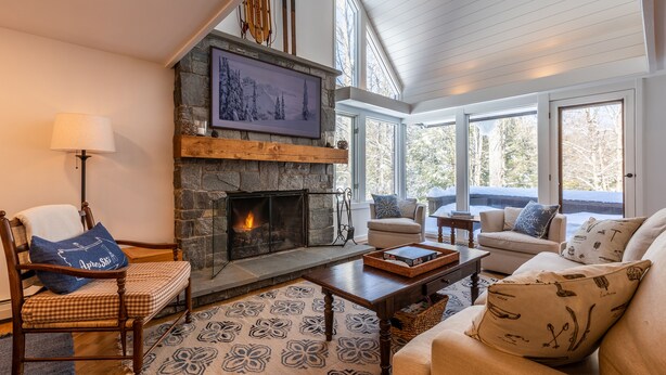 A cozy living room with a stone fireplace, comfortable seating, and large windows. - 2026 Seasonal Summer Rental (Winhall)