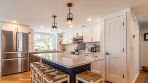 A modern kitchen with stainless steel appliances, a large island with bar stools, and pendant lighting. - 2026 Seasonal Summer Rental (Winhall)