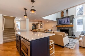 A spacious living area with a large island, a fireplace, and a view of the outdoors. - 2026 Seasonal Summer Rental (Winhall)