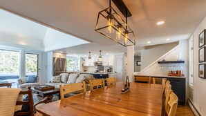 A spacious dining area with a wooden table and chairs, a kitchen in the background, and a staircase leading to another level. - 2026 Seasonal Summer Rental (Winhall)