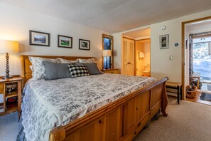 A bedroom with a large bed, wooden headboard, two bedside tables with lamps, a door leading to a balcony, and framed pictures on the wall. - 2026 Seasonal Summer Rental (Winhall)