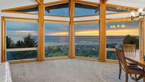 Et hjørneværelse med store vinduer, der giver udsigt over havet og en solnedgang.