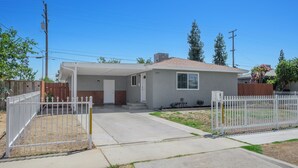 A single-story house with a covered porch, a fenced yard, and a clear blue sky.