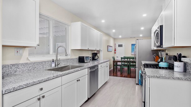 A modern kitchen with white cabinets, granite countertops, a dishwasher, a microwave, and a stove. There is a dining area with a table and chairs.