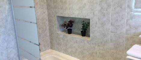 A bathroom with a bathtub, a glass shower enclosure, and two potted plants on a shelf.