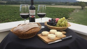 Ein Tisch mit einer Weinflasche, zwei Gläsern, einem Brotlaib, einer Weintraubenkörbchen und einem Schneidebrett mit Käse.