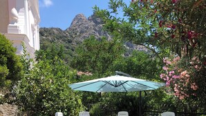 Eine Terrasse im Freien mit Steinböden, weißen Lounge-Stühlen, einem Holztisch und einem großen Sonnenschirm.