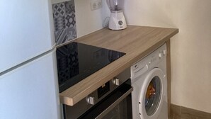 Eine kleine Küche mit Einbauofen, Waschmaschine und Mixer auf der Arbeitsfläche.
