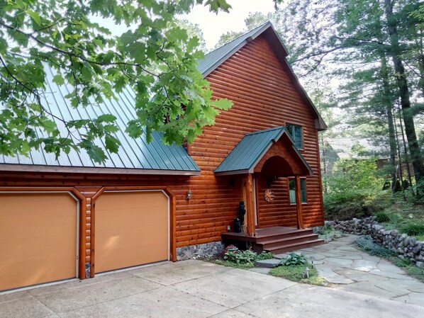 A log cabin with a garage, a stone pathway, and a stone wall.