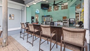 Zona bar con sgabelli alti, un bancone con un rubinetto per bevande, una ventola a soffitto e un televisore fissato al muro.