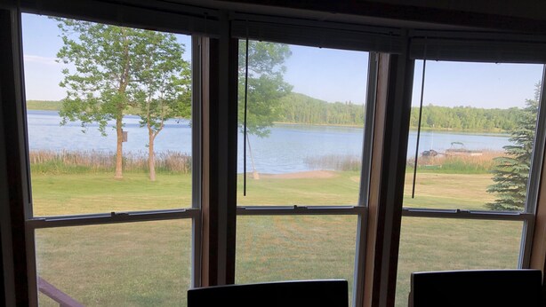 Une pièce dotée de grandes fenêtres donnant sur un lac, de deux fauteuils et d’une table en bois.