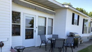 Une maison mobile dotée d’un patio comprenant une table et des chaises, un barbecue et un drapeau américain.