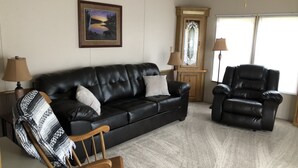 Un salon avec un canapé en cuir noir, une chaise en bois, un fauteuil en cuir noir, deux lampes et un tableau encadré accroché au mur.