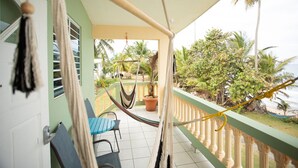 A balcony with a hammock, a potted plant, and a view of palm trees and the ocean.