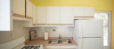 A compact kitchen with white cabinets, a gas stove, a sink, and a refrigerator.