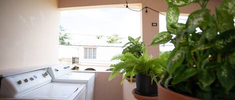 A laundry area with a washing machine and dryer, a window with a view of buildings, and potted plants.