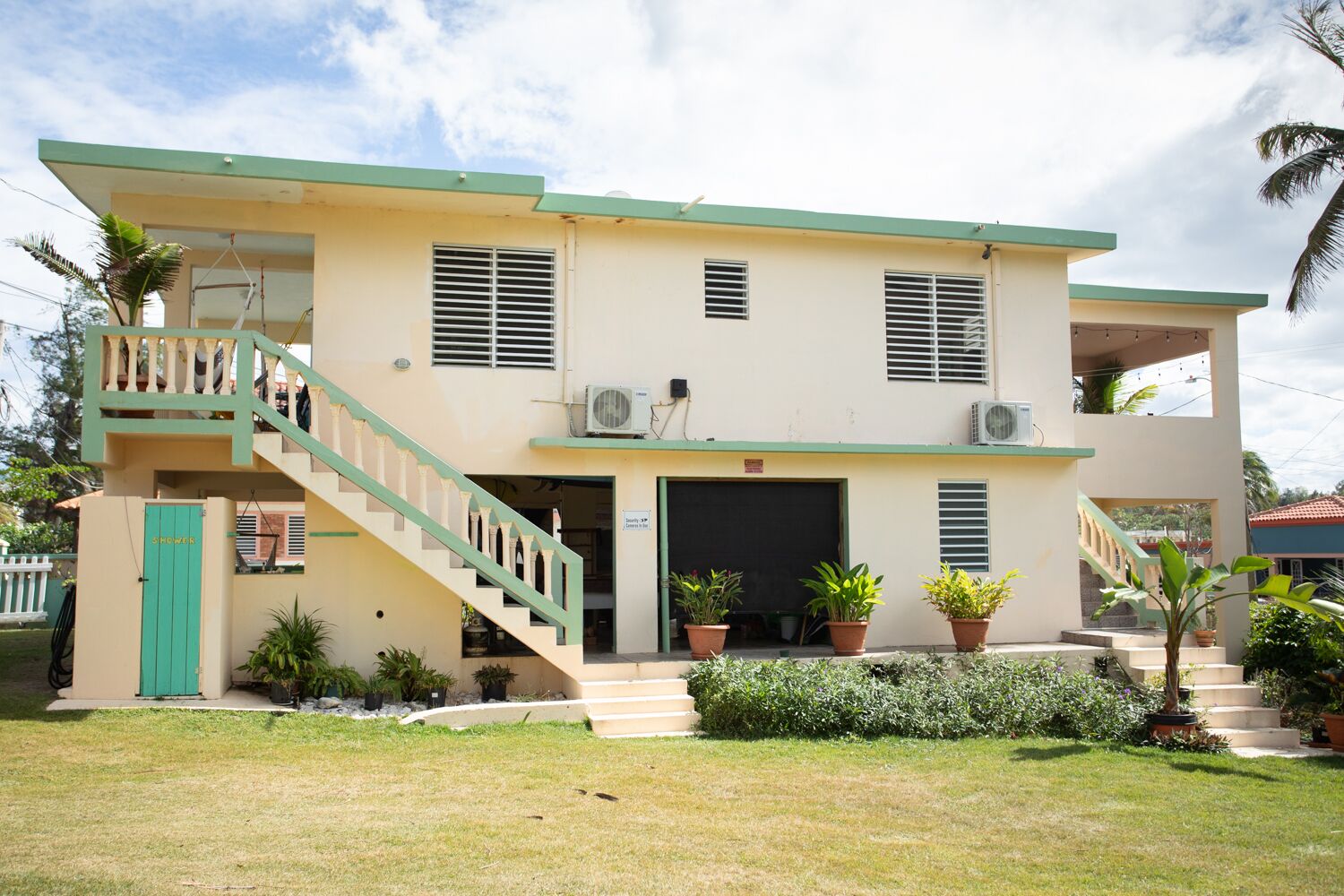 A two-story building with a green staircase, multiple air conditioning units, and potted plants.