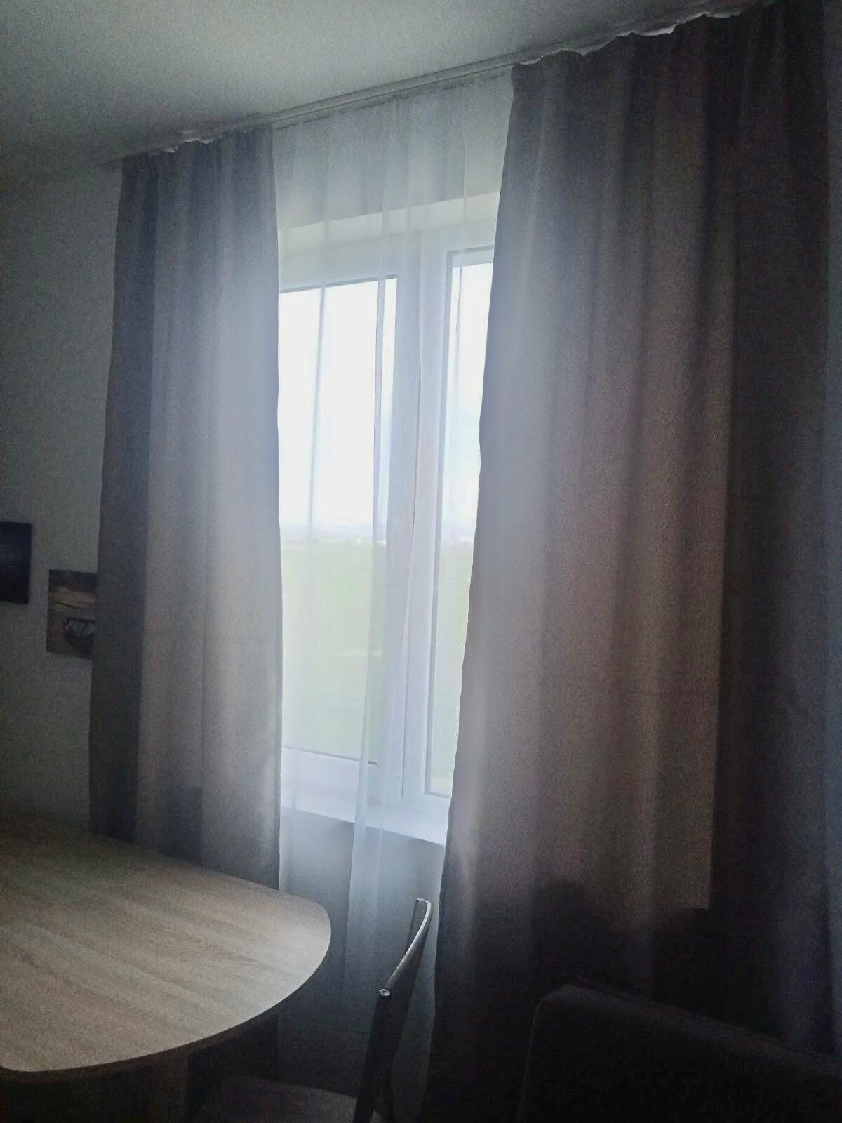Ett rum med ett runt bord, två stolar och ett fönster med tunna, genomskinliga gardiner.