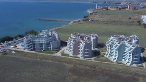 A coastal hotel with multiple buildings, a parking area, and a view of the sea. - 1-bed Modern Sea View Apartment in Aparthotel (Pomorie)