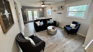 A spacious living room with a dark brown sofa, a blue armchair, and a round ottoman. There is a dining area in the background with a white table and chairs. - JOMO TriTerrace Enjoy Family, Relax Lakefront, Lake View, Priv dock Boat Slip (Rocky Mount)